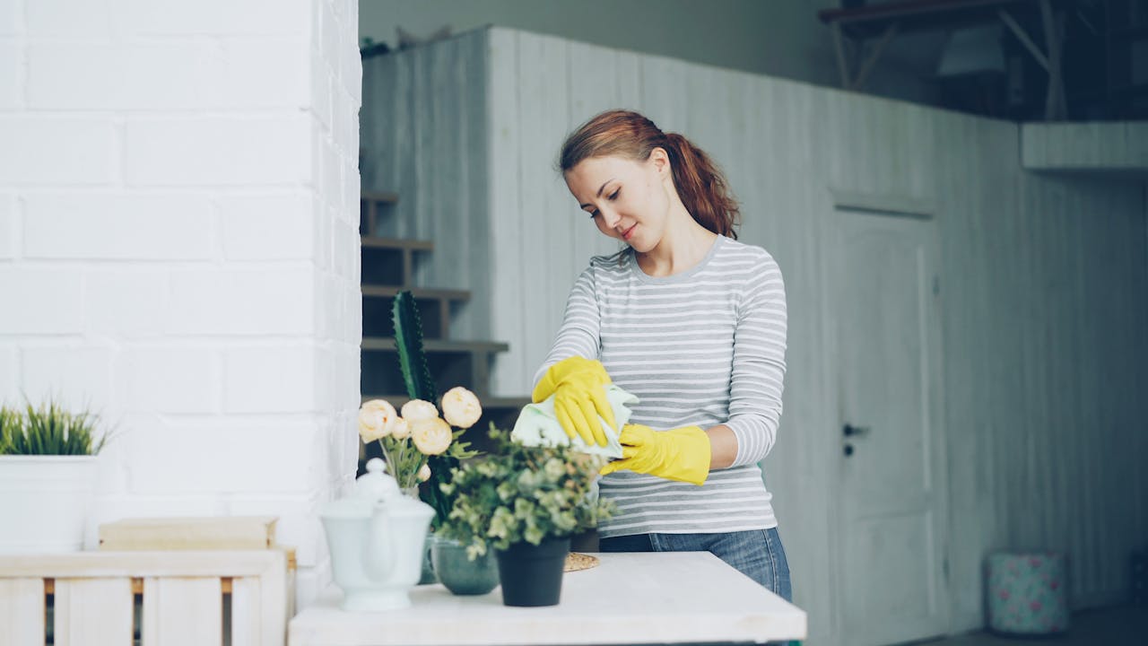 Young woman cleaning home with yellow gloves and striped shirt, focused on tidying indoors.