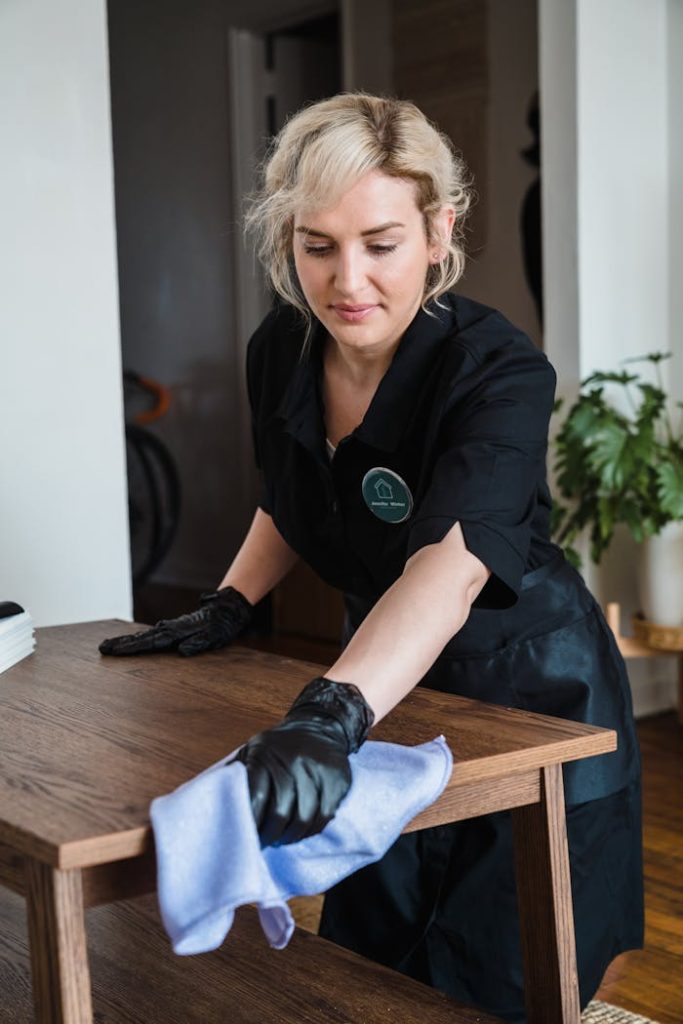 pexels photo 9462732 A housekeeper in uniform cleans a wooden table with a cloth, promoting cleanliness and care.